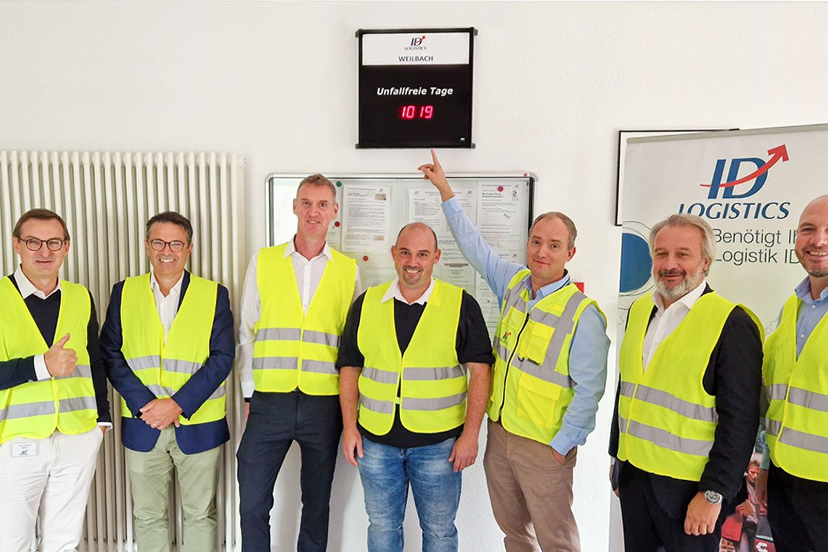 Smiling ID Logistics employees Eric Hémar and Christophe Satin with ID Logistics employees and a day counter without an accident.